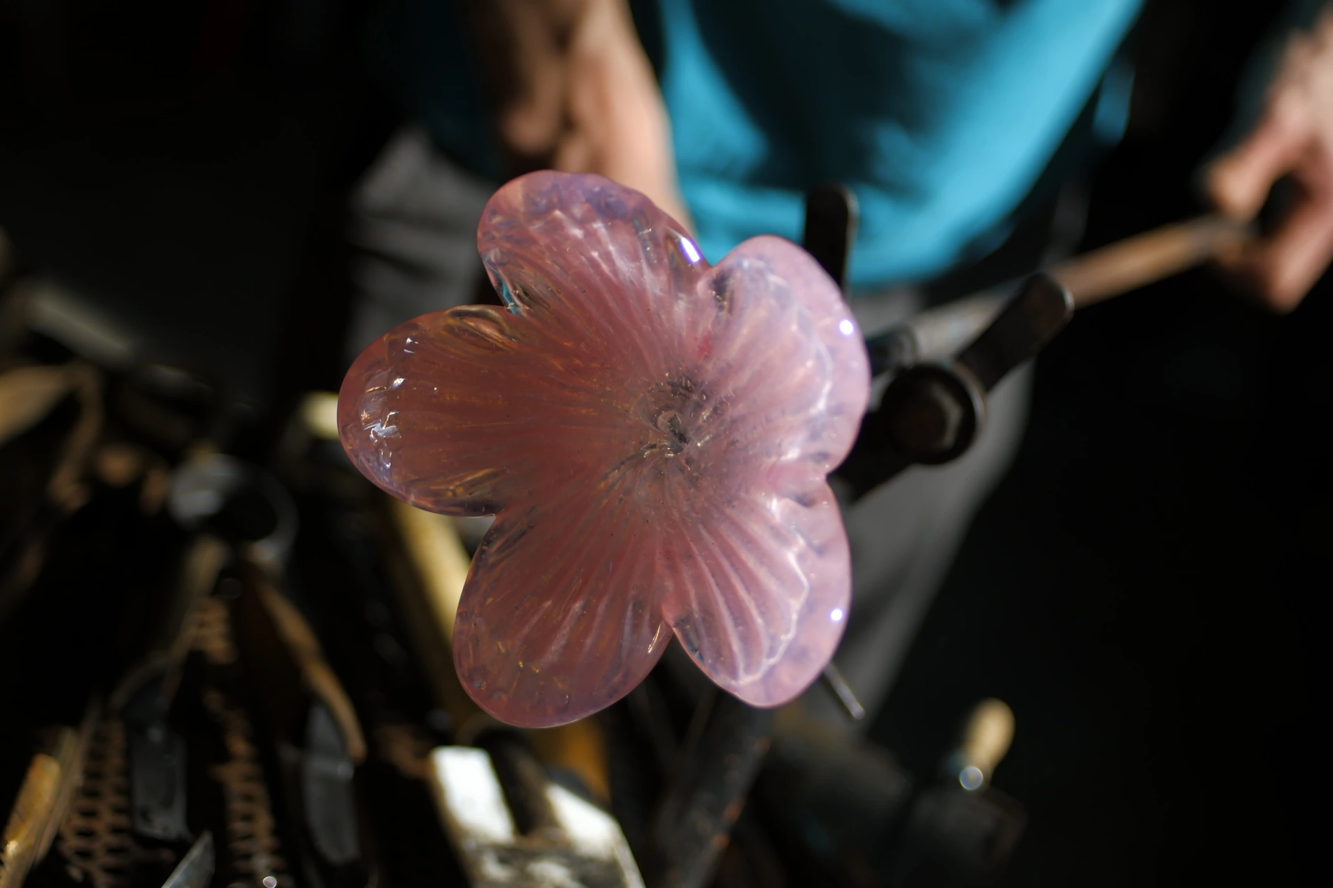A craftsperson shaping a pink glass blossom