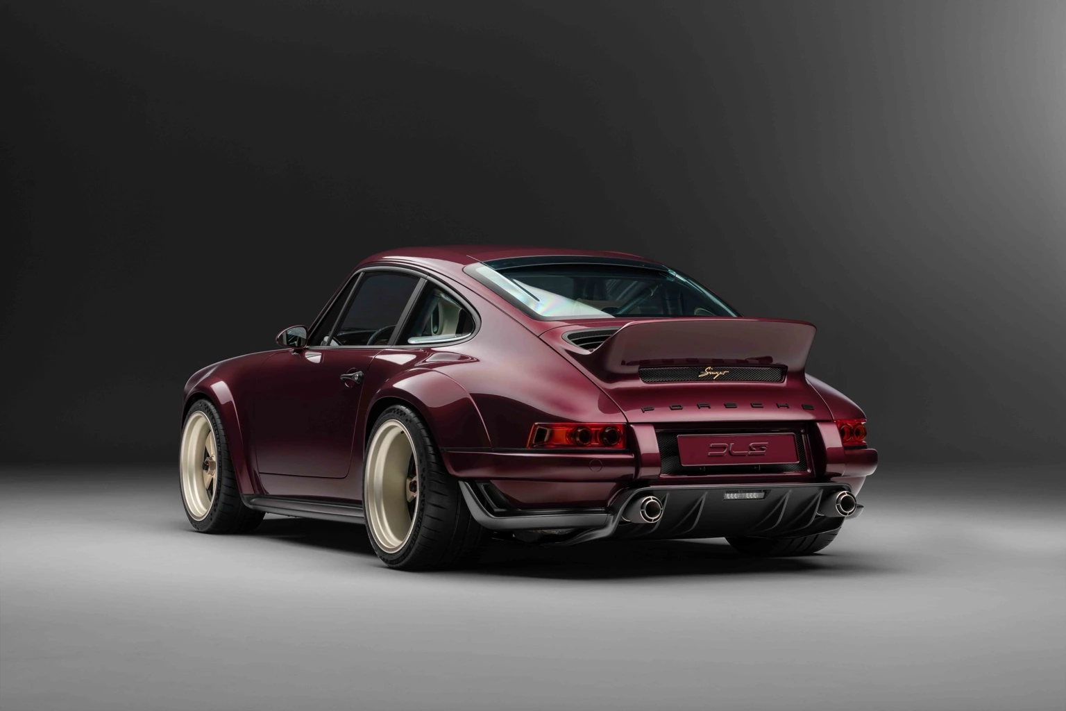 Rear three-quarter view of a burgundy Singer-restored Porsche 911 in a dark studio